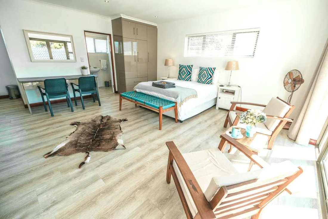 Bright Hermanus Reefs studio bedroom with white linen, teal pillows, wooden armchairs, a desk, and an ensuite doorway. Bright Hermanus Reefs studio bedroom with white linen, teal pillows, wooden armchairs, a desk, and an ensuite doorway.
