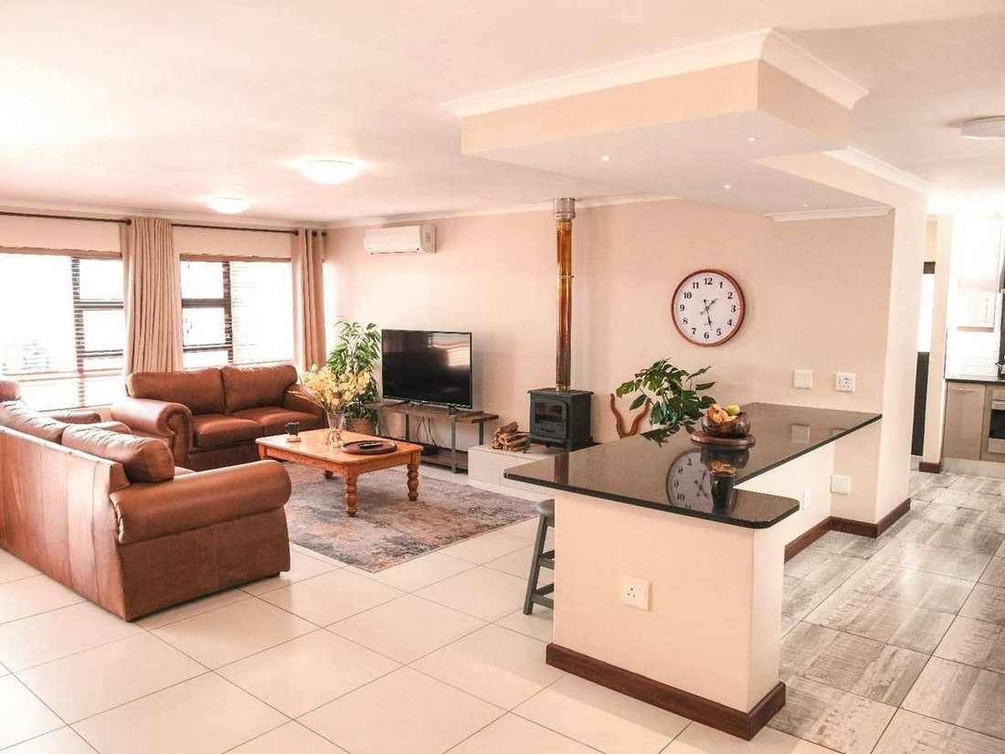 Whale Apartment living room at Hermanus Reefs with leather sofas, a wood stove fireplace, TV, and granite breakfast bar.