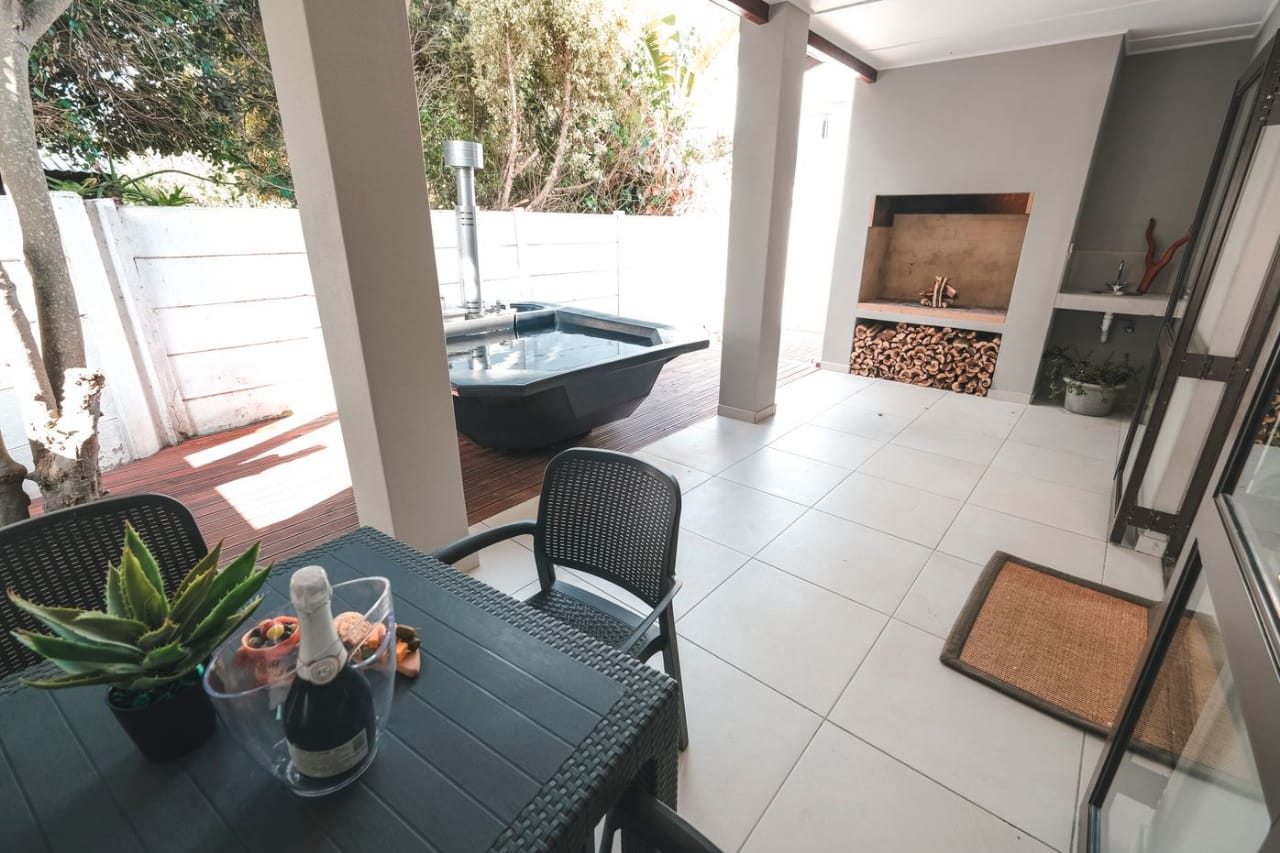 Covered patio dining table beside a built-in braai and wood-fired hot tub (Bamboo Apartment)