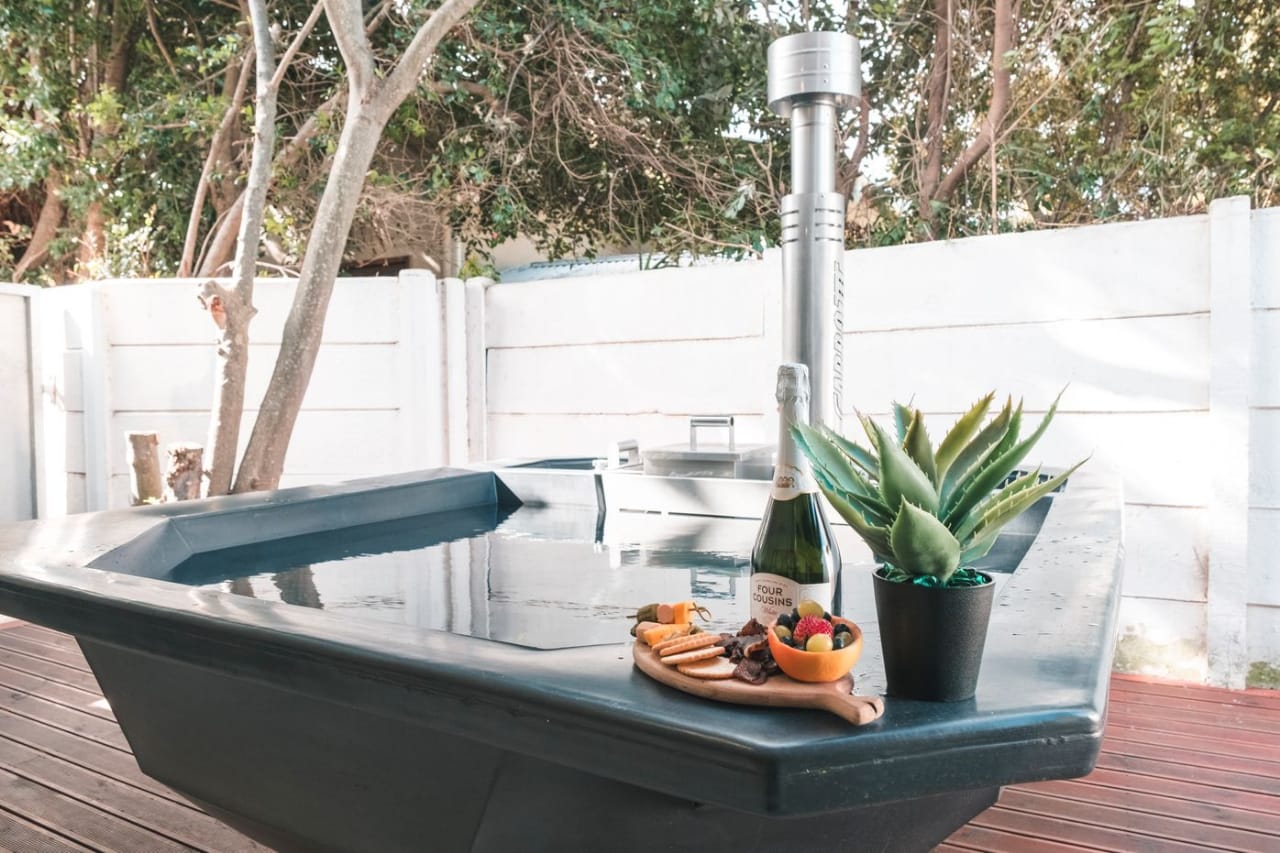 Wood-fired hot tub (Bamboo Apartment) on a wooden deck set with sparkling wine and a snack platter